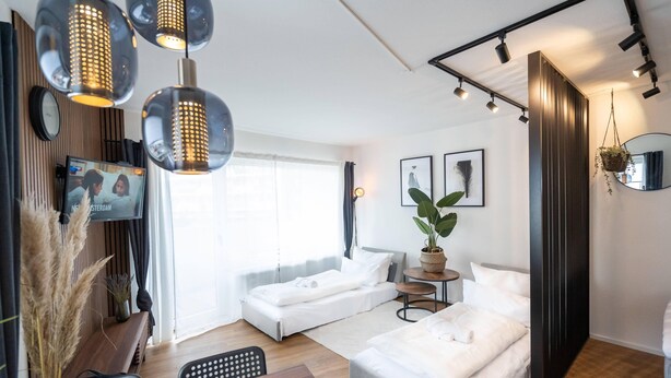 Una habitación de hotel moderna con cama, mesitas de noche, televisor y un amplio ventanal.