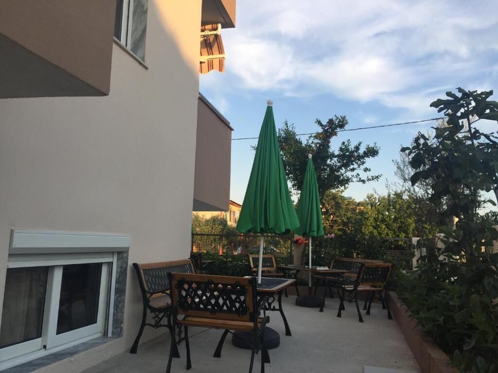 Un espace extérieur aménagé avec des tables et des chaises, des parasols verts et une vue sur les arbres et les bâtiments environnants.