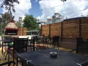 An outdoor patio with metal tables and chairs, a brick barbecue, and a wooden fence.
