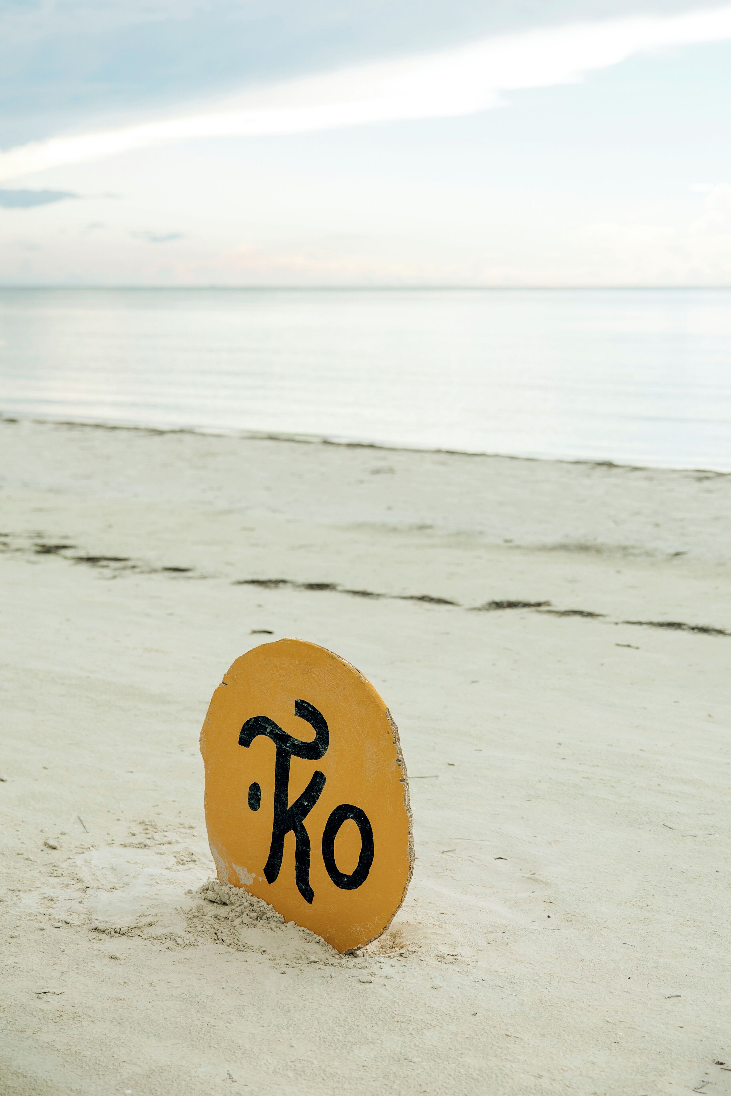Um sinal amarelo com texto preto numa praia de areia.