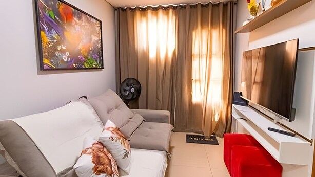 A living room with a sofa, a TV, a red chair, a fan, and a window with curtains. - OZPED Flats Particulares Casa Cruzeiro (Cruzeiro)