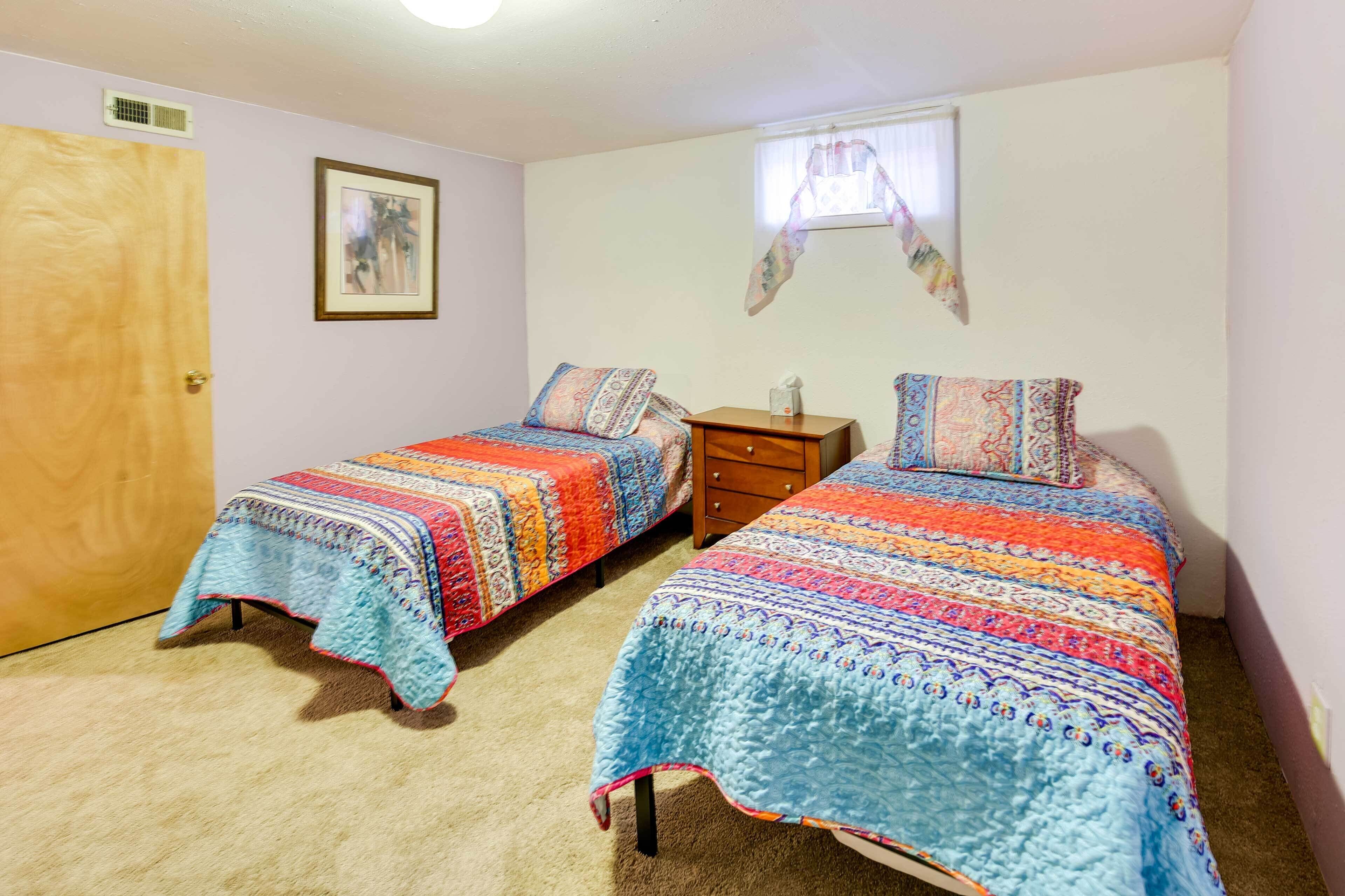 A bedroom with two single beds, a wooden door, a small dresser, and a window with a curtain.