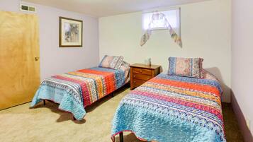 A bedroom with two single beds, a wooden door, a small dresser, and a window with a curtain.