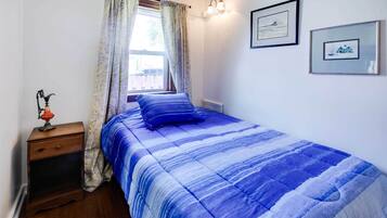 Una camera da letto con un letto, un comodino, una finestra con tende e due quadri appesi al muro.