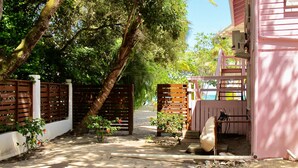 A pathway leading to a pink building with a wooden gate, surrounded by lush greenery and trees.
