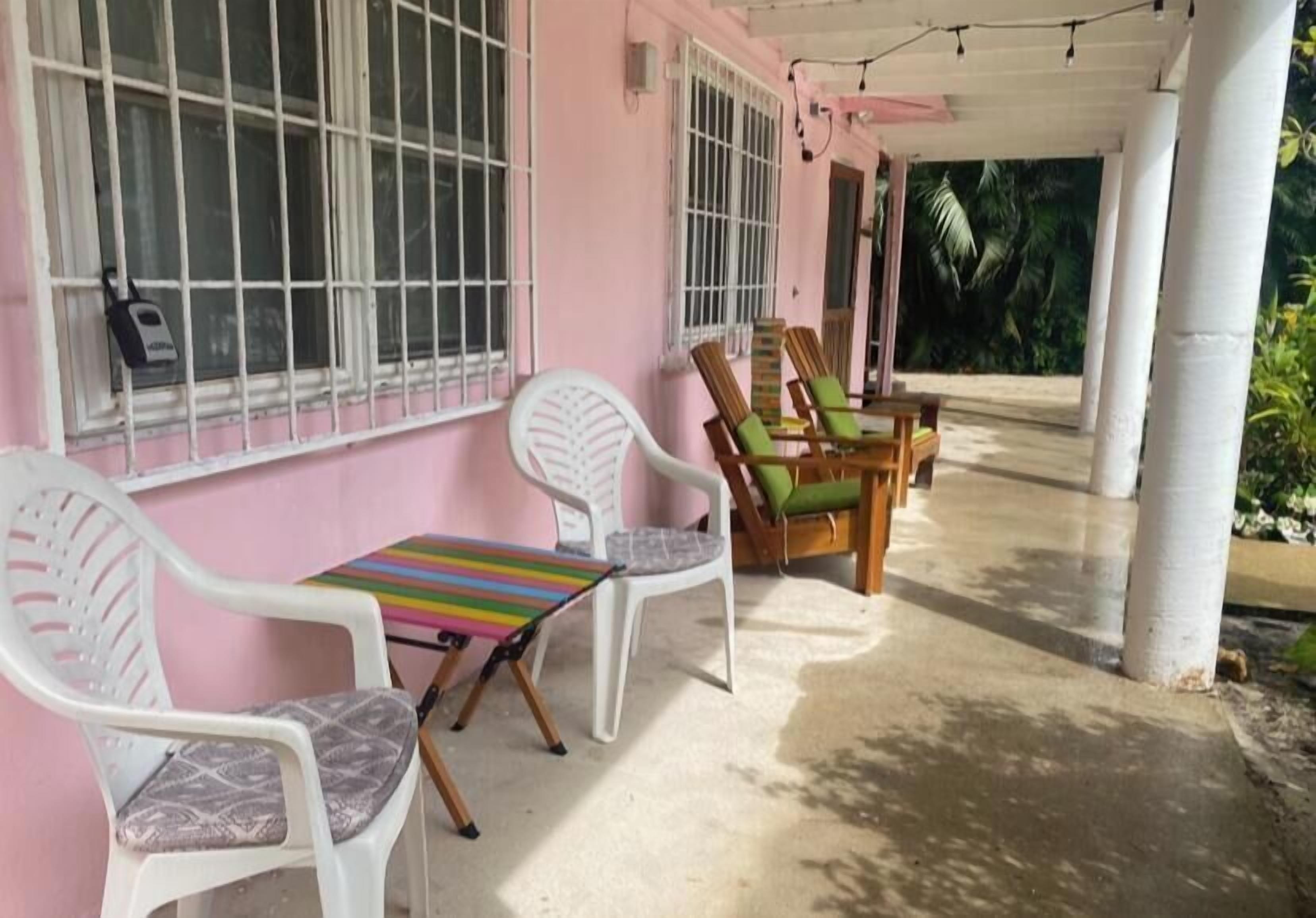 A pink building with barred windows, a covered outdoor seating area with a table and chairs, and a concrete floor.