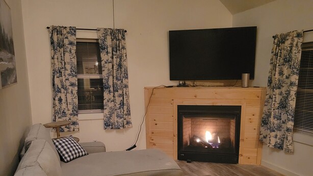 Een gezellige woonkamer met een open haard, een bank, een salontafel en een televisie boven de open haard.