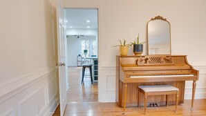 A piano with a bench, a mirror, and a potted plant in a room with wooden flooring and a patterned rug. - Private Party House - Forest Masters Retreat (Evans)