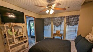 A bedroom with a large bed, a ceiling fan, a TV, and a rustic wooden shelf.