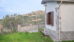A stone house with a balcony, a stone wall, and a view of a hillside town.