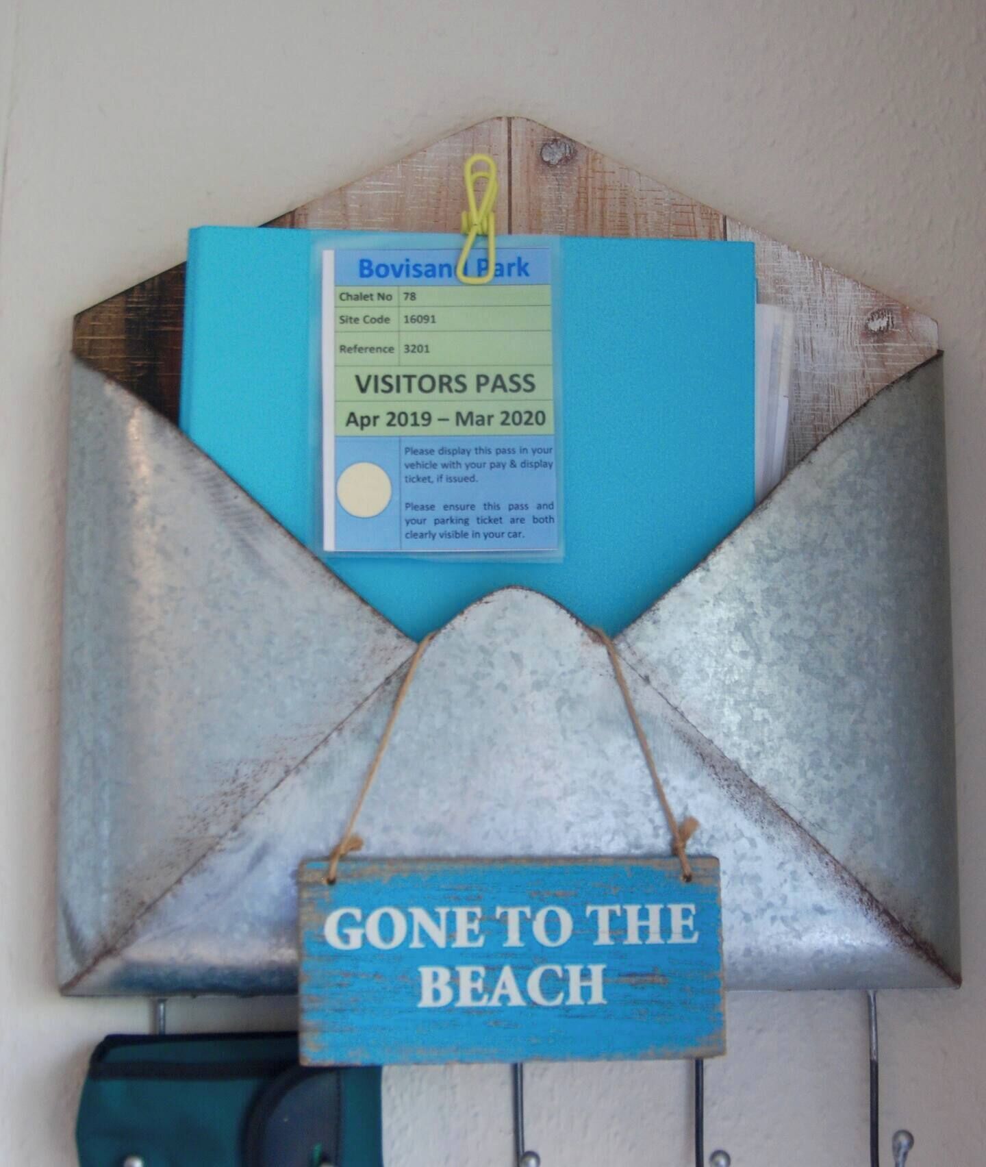Un objet décoratif fixé au mur, comprenant un badge de visiteur et une pancarte sur laquelle on peut lire : « JE SUIS À LA PLAGE ».