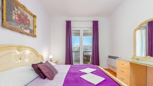 Een slaapkamer met een bed, nachtkastje, dressoir, spiegel en uitzicht.