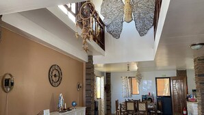 Un vestíbulo amplio con techo alto, un gran reloj de pared, una mesa de recepción y un área de comedor con sillas y mesas de madera.