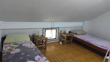 A dormitory room with a bed, a desk, a chair, a small table, a window, and a bunk bed.