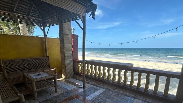 Un patio frente a la playa con un banco y una mesa de madera, suelo de baldosas y vista al océano.