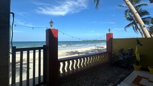 Vista de la playa desde un porche con barandilla, palmeras y cielo despejado.