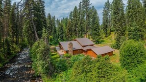 Eine Holzhütte mit einem Steinkamin, umgeben von dichtem Wald und einem Bach.