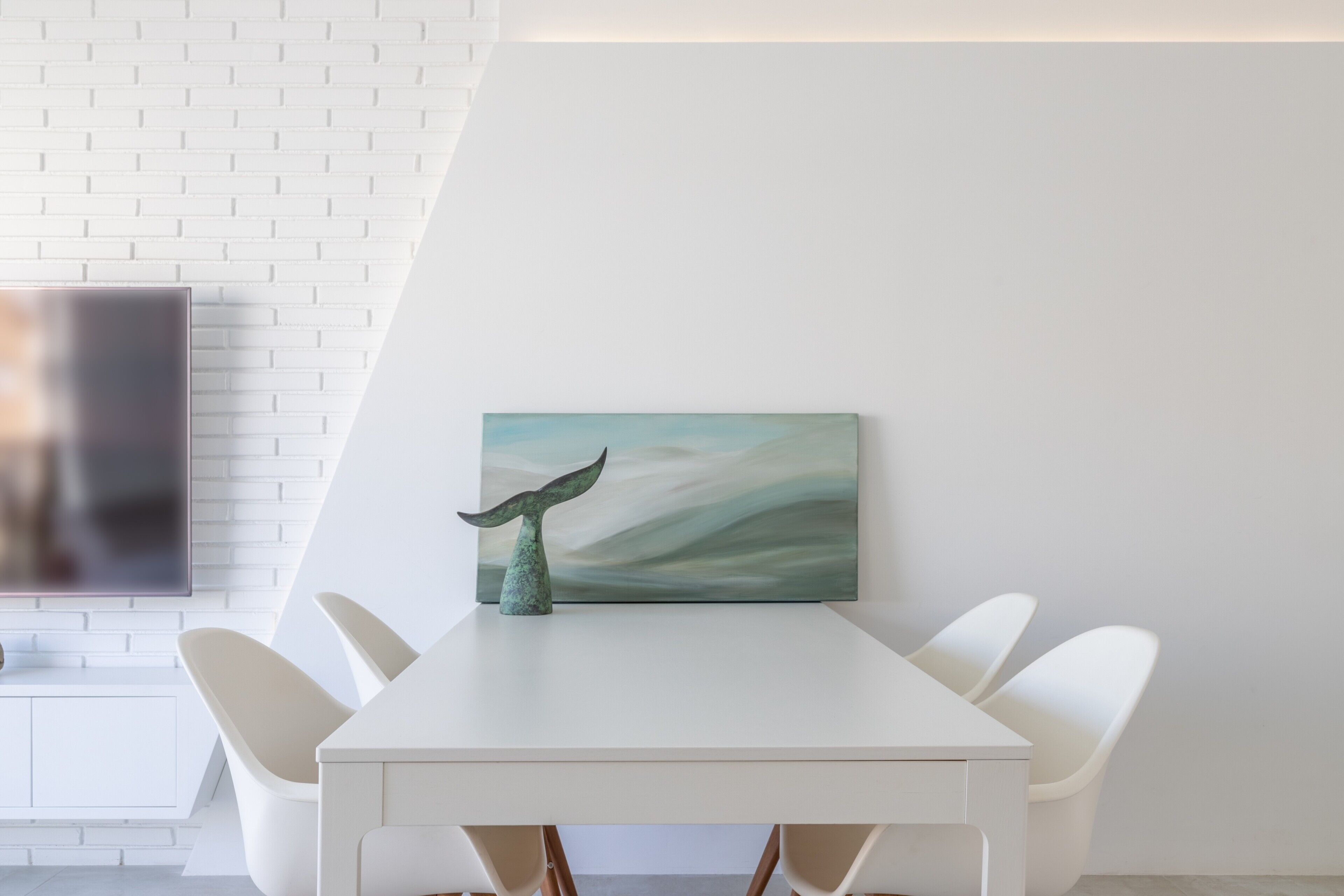Een moderne eetruimte met een witte tafel, stoelen en een wanddecoratie.