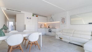 Una cocina moderna con armarios blancos, un comedor con mesa y sillas blancas, y un sofá blanco en la sala.