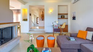 A living room with a fireplace, a sofa, a coffee table, and a staircase leading to another room. - Villa 'Margarita's 2' with Sea View, Wi-Fi and Air Conditioning (Chania)