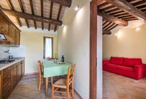 Une cuisine avec des meubles de rangement en bois, une table à manger avec des chaises, un canapé rouge et un sol carrelé.
