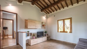 A spacious living area with a wooden floor, a built-in TV stand, and a sofa. - Apartment 'Faetino - Gallo' with Shared Pool, Private Garden and Wi-Fi (Colle di Val d'Elsa)
