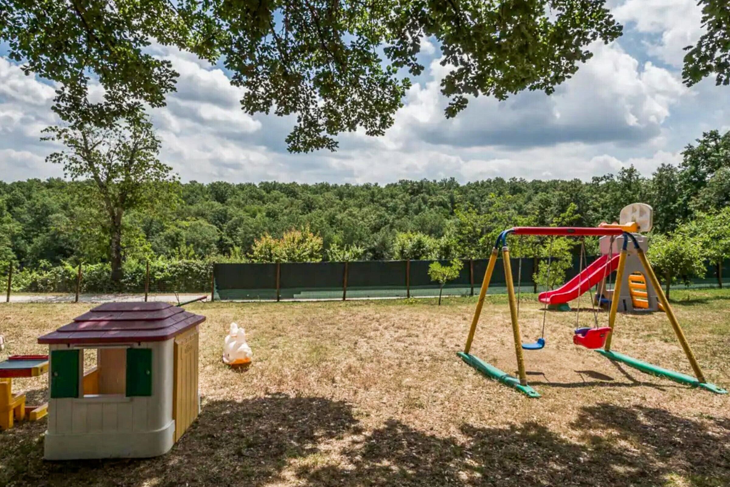 A playground with a swing set and slide, surrounded by trees and a fenced area.