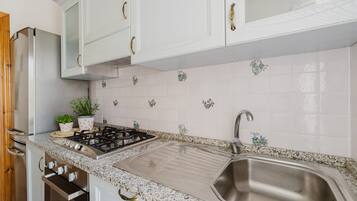 A kitchen with white cabinets, a stainless steel sink, a gas stove, and decorative tiles.