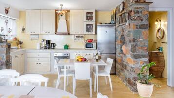A kitchen with white cabinets, a stone wall, a refrigerator, and a dining table with chairs.