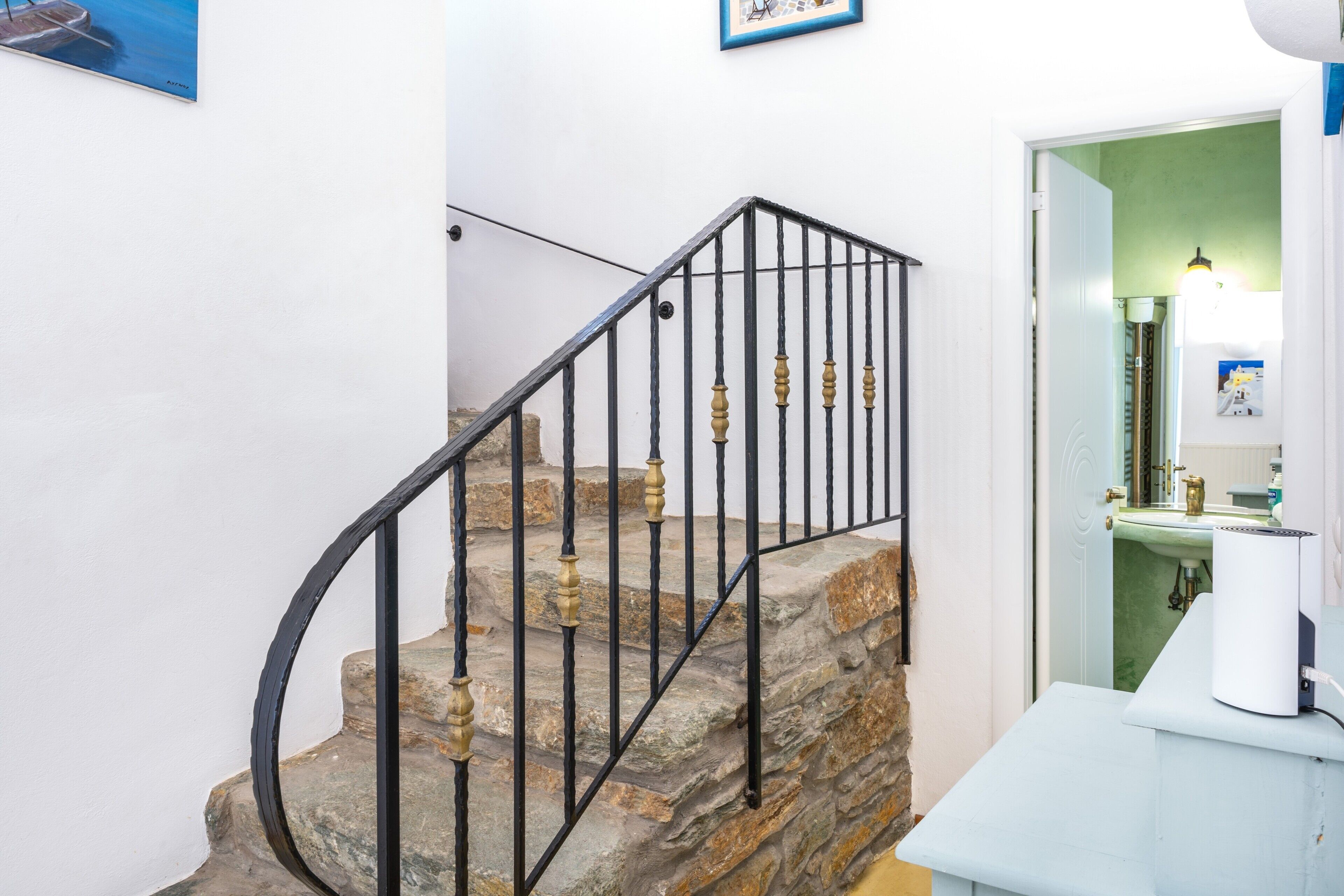 A staircase with stone steps and black metal railings, leading to a room with a green wall and a white sink.