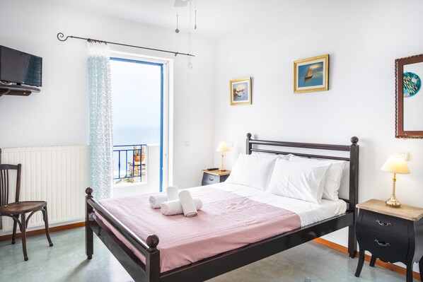 Ein Schlafzimmer mit Bett, Sessel, Nachttisch, Lampe, Fernseher und Fenster mit Blick.