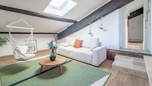 Une pièce de style loft avec un canapé blanc, un fauteuil suspendu, une table basse en bois et une lucarne.