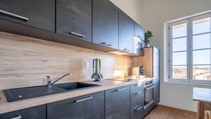 Une cuisine moderne avec des meubles de couleur sombre, un plan de travail en bois, un évier et une fenêtre donnant sur un paysage agréable.