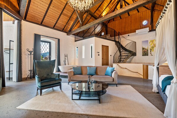 A spacious living area with a high wooden ceiling, a staircase, and a large window. - Apartment 'Thanhammer Quarz' with Mountain View, Pool and Air Conditioning (Terlano)