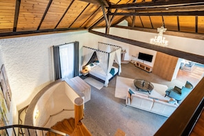 Ein Zimmer mit hohen Decken, einem Bett, einer Sitzecke und einem Fernseher.