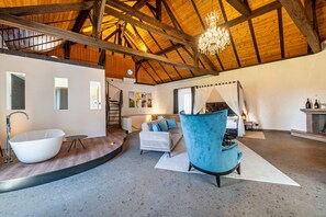 Ein geräumiges Zimmer mit einer großen Badewanne, einem blauen Sessel, einem Sofa und einem Kamin.
