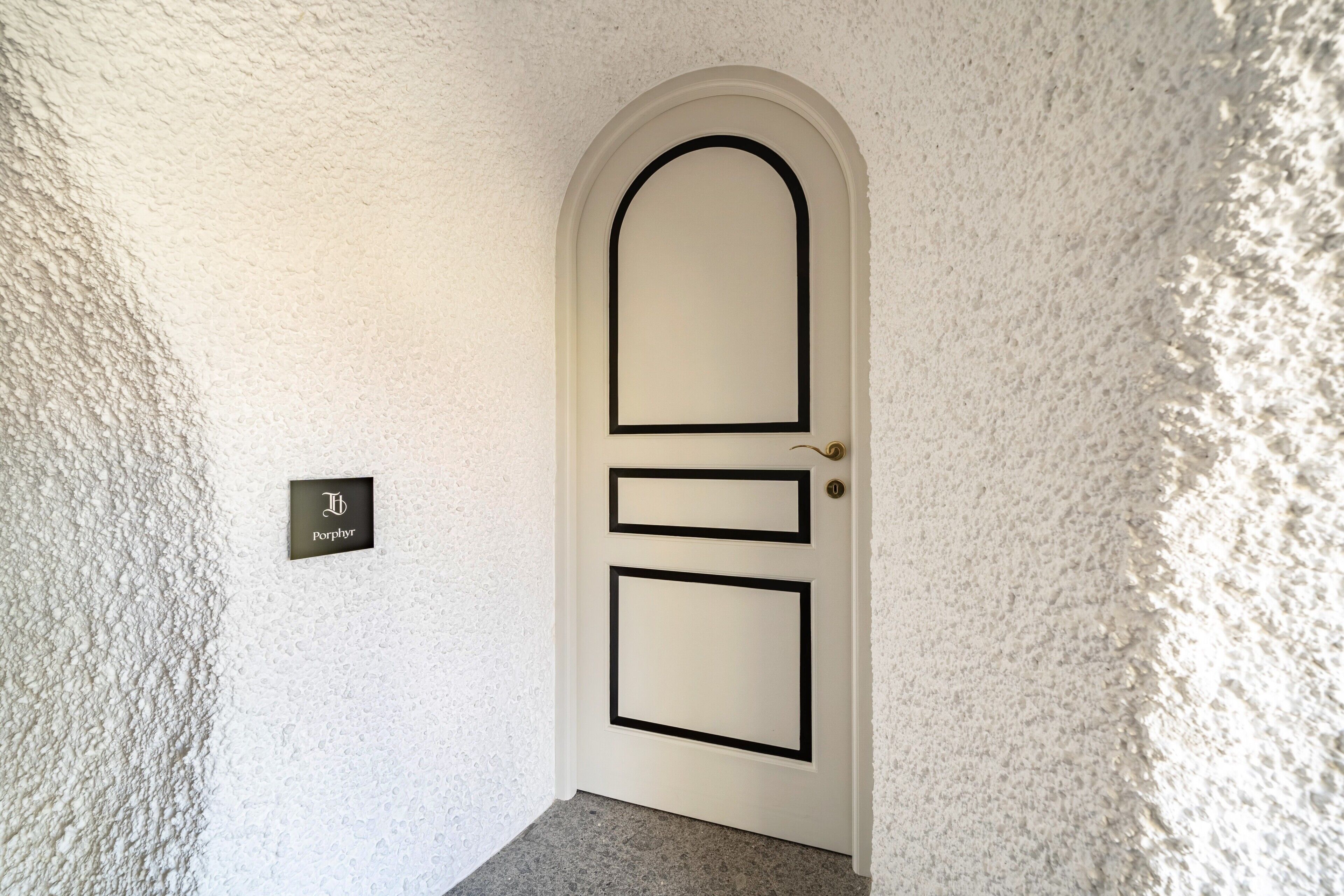 A white door with a black frame and a rectangular panel, a doorbell, and a sign with the text 'Porphor' on the wall.