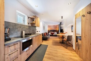 A modern kitchen with wooden cabinets, a built-in oven, and a dining area with a table and chairs. - Apartment 'Thanhammer Porphyr' with Mountain View, Shared Terrace and Pool (Terlano)