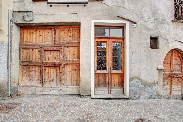 Un bâtiment doté de grandes portes en bois, d’une petite fenêtre ornée de barreaux en fer forgé et situé sur une rue pavée.