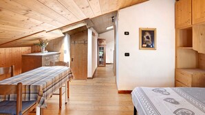 A room with wooden walls and ceiling, a bench, a bed, and a small table with a vase. - Studio Apartment 'Premesan 2' with Mountain View and Wi-Fi (Bormio)