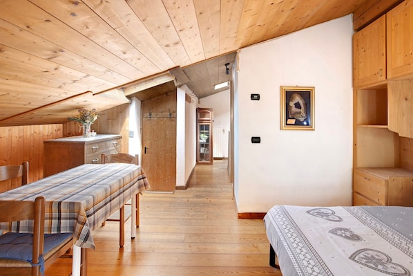 Ein Zimmer mit Holzwänden und -decken, einer Sitzbank, einem Bett und einem kleinen Tisch mit einer Vase.