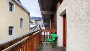 Ein Balkon mit Holzgeländer, einem grünen Stuhl und Blick auf angrenzende Gebäude.