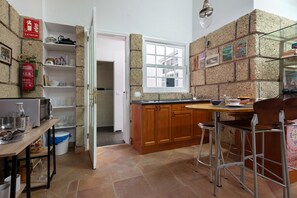 A kitchen with a stone wall, wooden cabinets, a sink, and a dining area with metal chairs. - Vacation Apartment 'Loft  Parque Santa Cruz' with Shared Terrace and Wi-Fi (Santa Cruz de Tenerife)