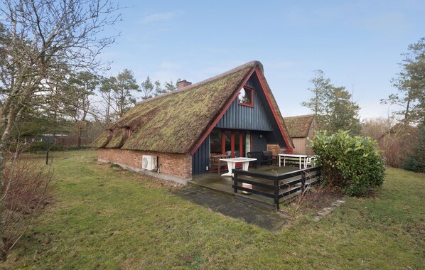Une petite maison au toit de chaume, dotée d  ’une terrasse en bois et d’une table avec des chaises à l’extérieur.