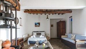 A room with a bed, a sofa, a table, and a stone floor. - Olive Guesthouse Junior Apartment with Sea View and Wi-Fi (Andros island)