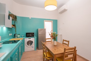 A compact kitchen with a washing machine, microwave, and a dining area with a table and chairs.