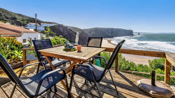 Una terraza de madera con una mesa y sillas que da a vistas de la costa.