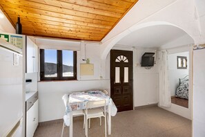 Ein Zimmer mit Holzboden, einem Fenster mit Bergblick, einem Tisch mit Stühlen, einer Tür und einem an der Wand befestigten Fernseher.