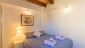 Un dormitorio con cama, mesita de noche, lámpara, un cuadro enmarcado y dos toallas sobre la cama.