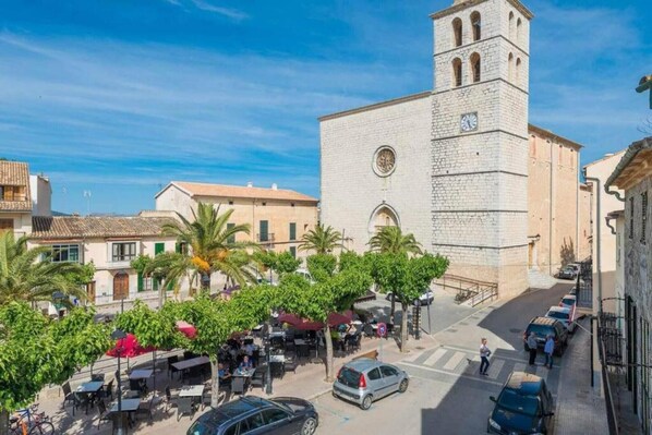 Una calle con un edificio destacado que tiene una torre del reloj, mesas al aire libre y coches aparcados.